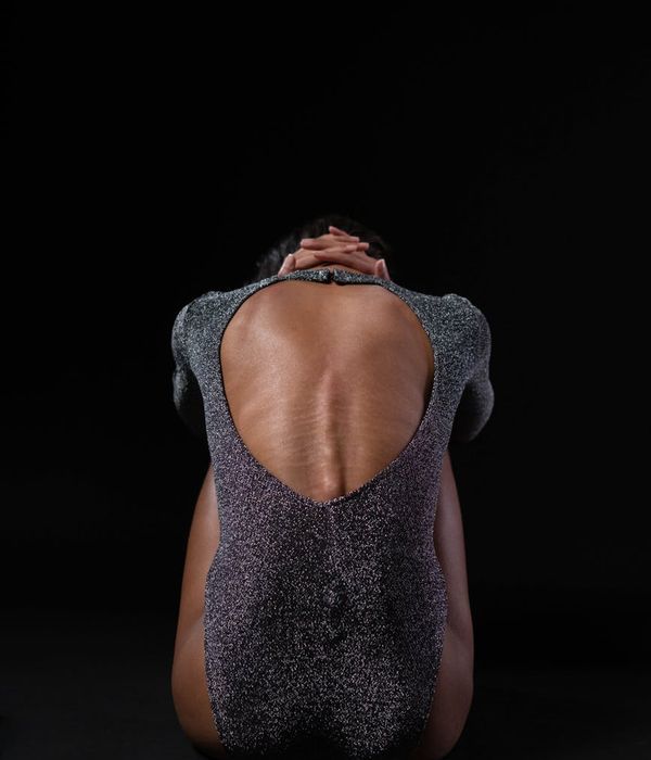Person in a balancing yoga posture against a dark background with cyan light.
